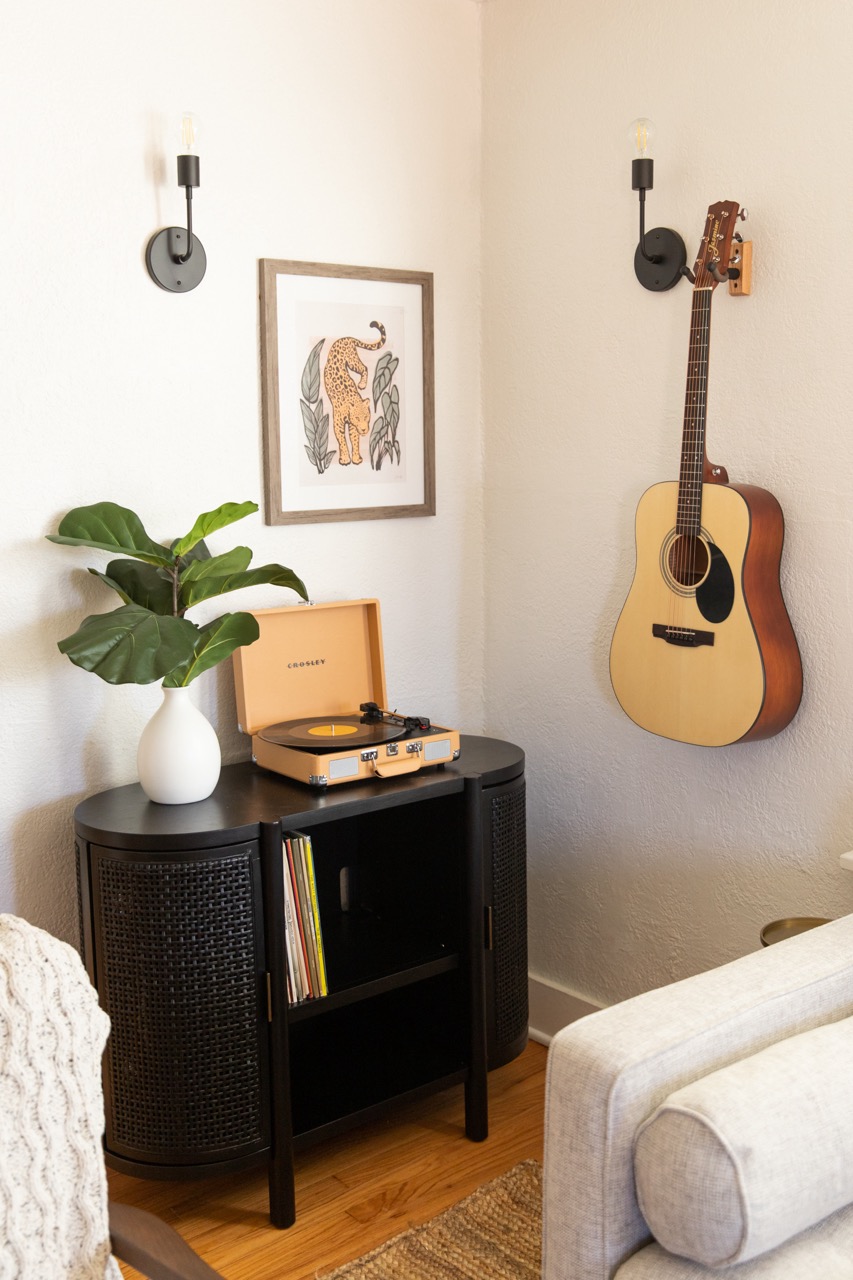 A corner of the living room of our Airbnb short-term rental decorated with a console table, record player, plant and guitar hanging on the wall.