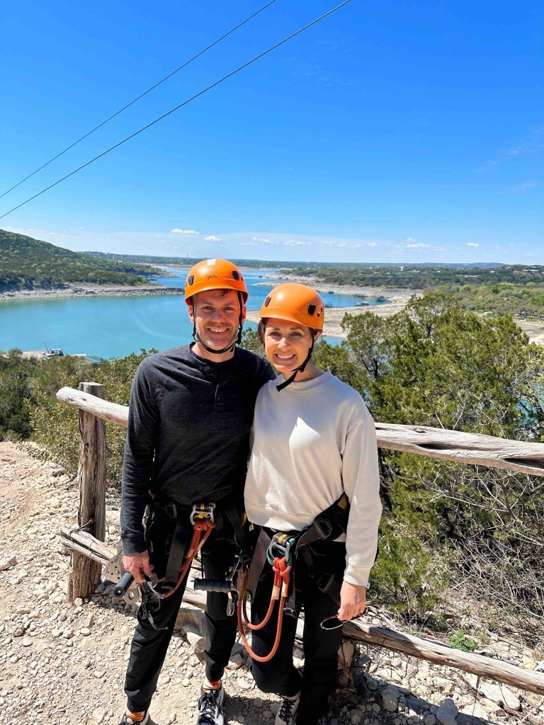 My husband and I in front of the beautiful scenery of Lake Travis with our ziplining helmets and harnesses.
