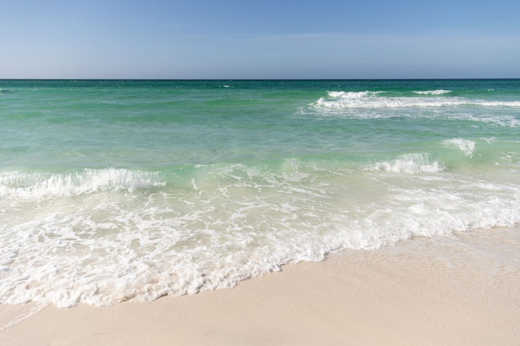 White sand beach with crashing waves in the turquoise water with a blue sky.