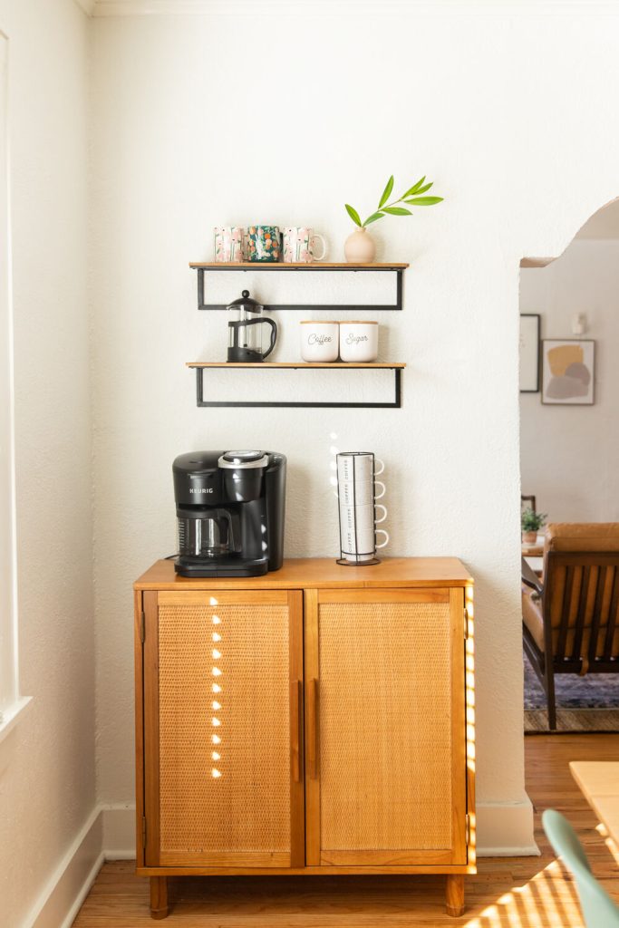A well organized Airbnb coffee station featuring a coffee maker, coffee grounds, sugar and designer mugs.