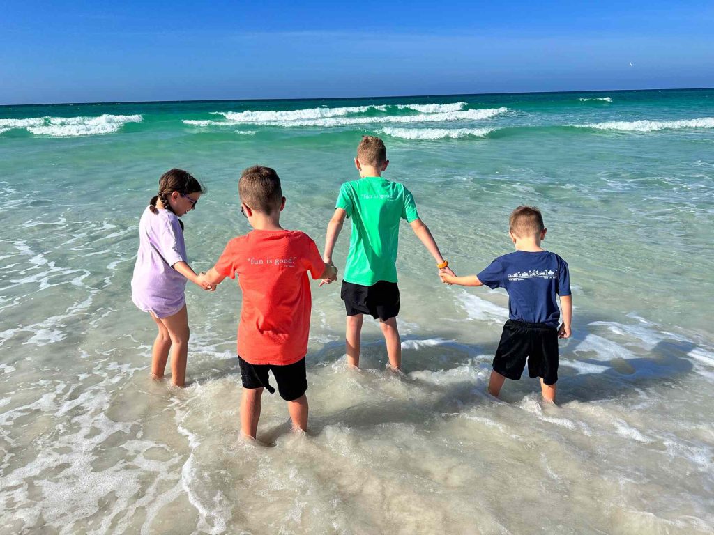 Our kids playing on the beach in 30A. They are holding hands as they walk in the water.