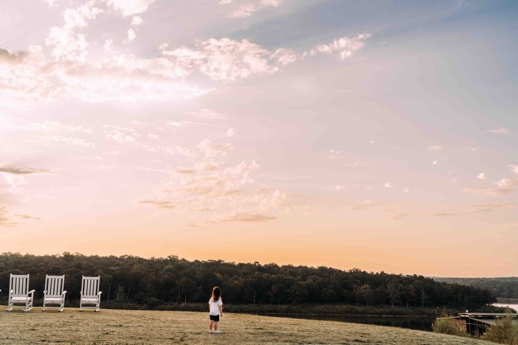 A toddler on a hill looking out over a pink and blue sunset.