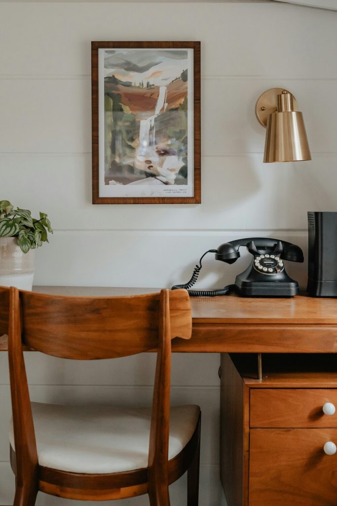 A vintage wooden desk with small plant and vintage phone on top. Adding a desk gives guests a space to work remotely.