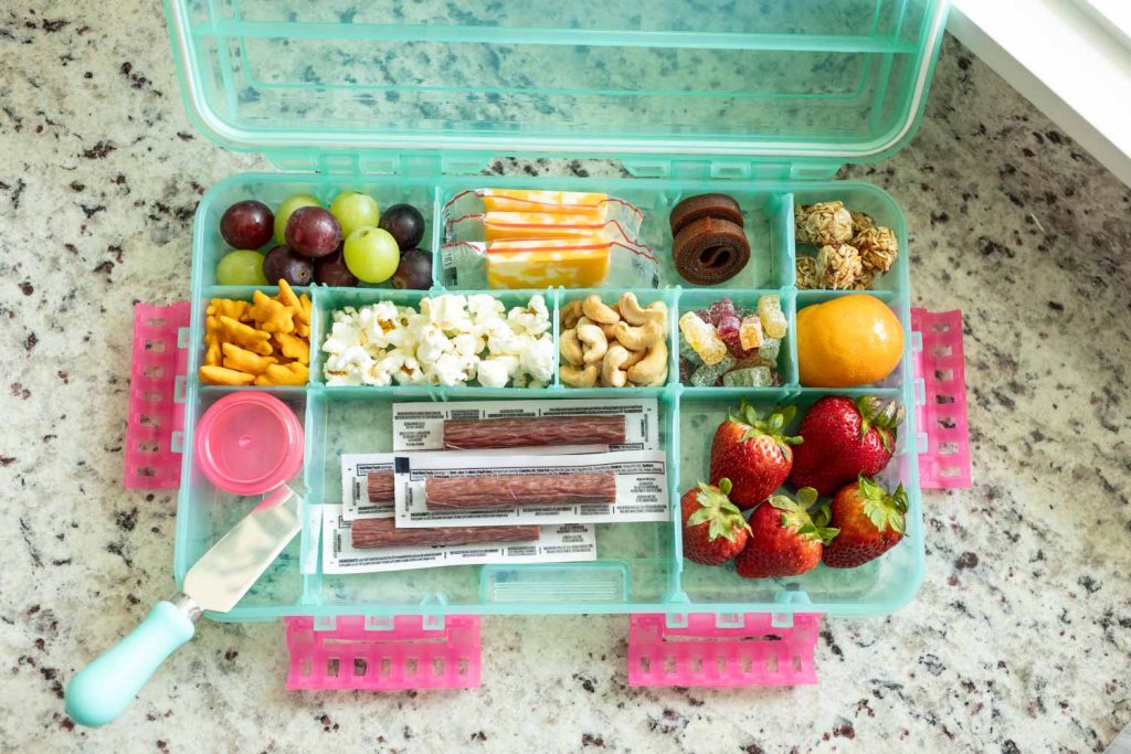 A teal snackle box filled with snacks like grapes, cheese, fruit rolls, granola balls, beef sticks and popcorn. We like to use a combination of sweet and salty snacks.