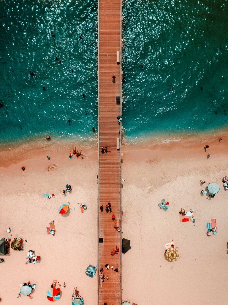 Birds-eye-view of Naples Pier–showing blue-green water and people relaxing on the beach.