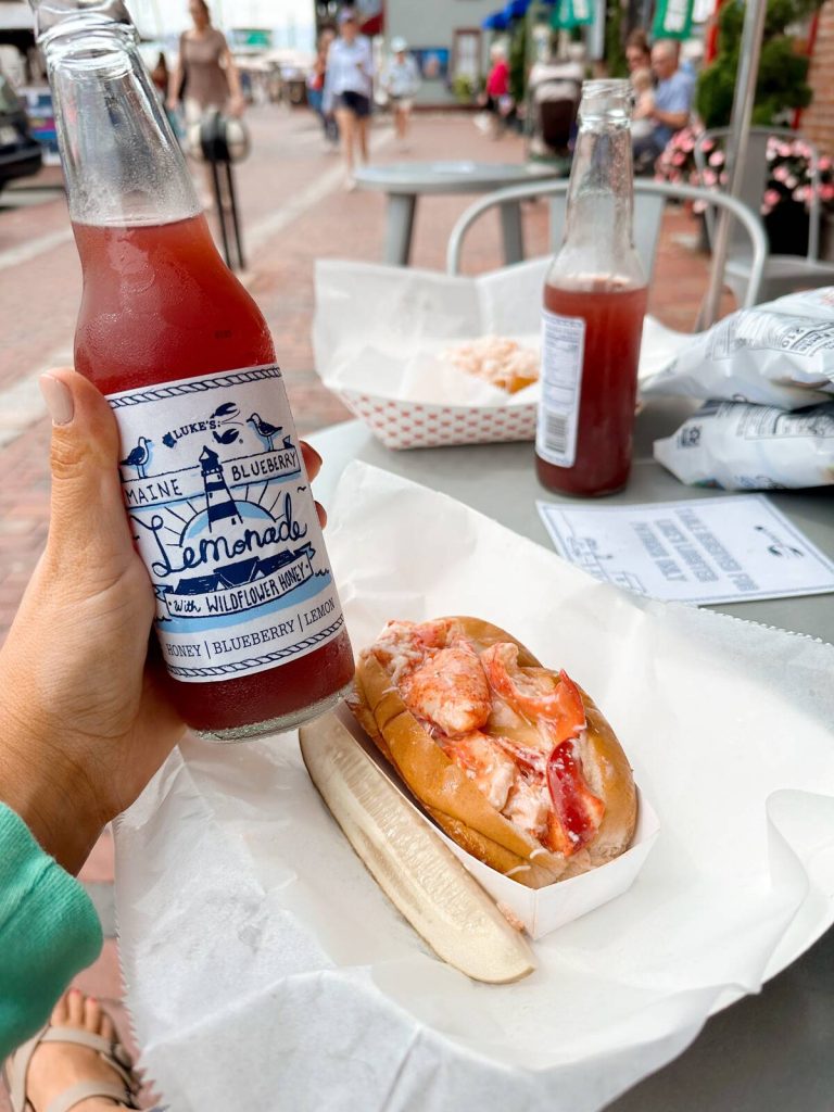 Me sitting at a table on Bowen's Warf with a lobster roll and lemonade from Luke's Lobster.