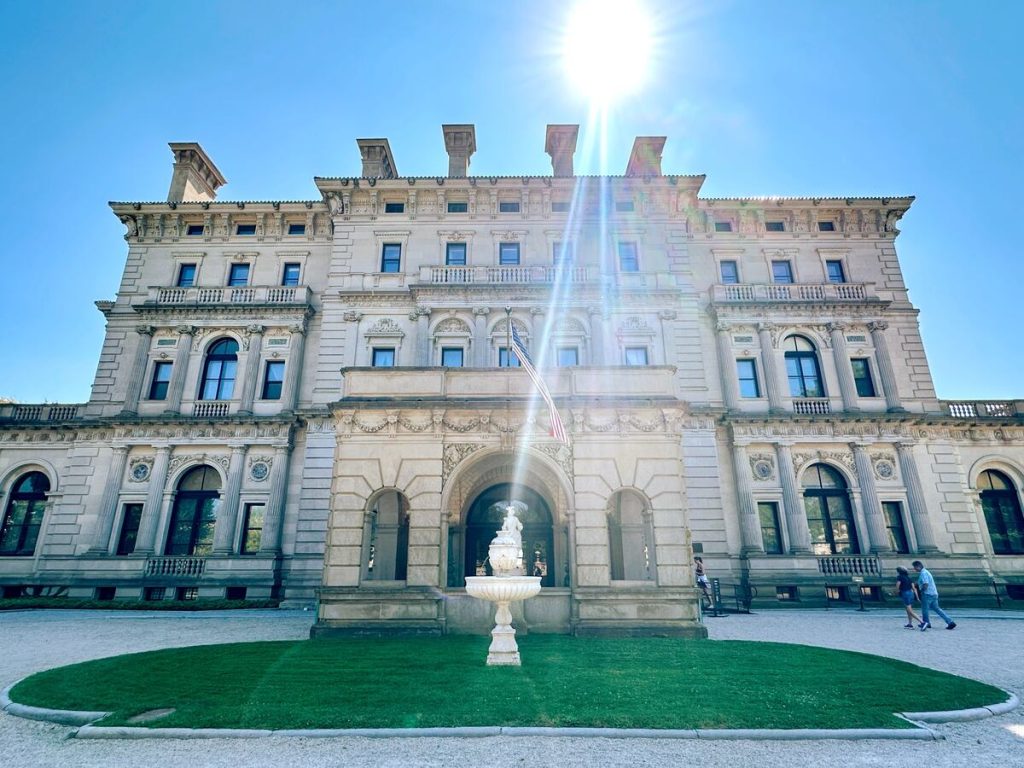 The front of The Breakers mansion in Newport with blue skies and manicured landscaping.