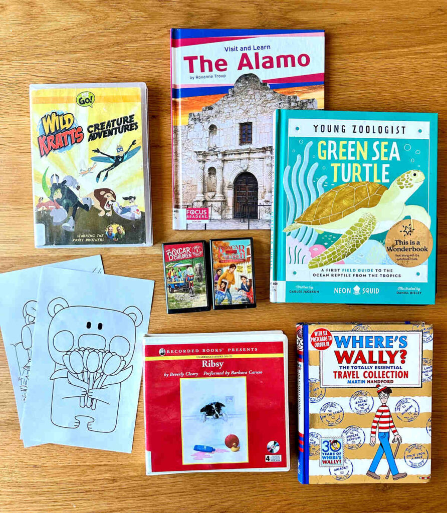 A flat lay of the library resources we check out before travel days. This free entertainment includes playaways, books on CD, coloring pages, DVDs and books.