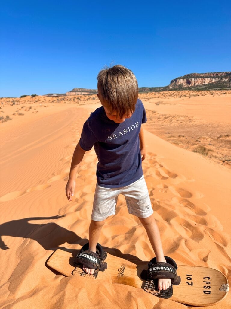 Our 7-year-old standing on a sandboard on the top of a small dune. He picked up sandboarding surprisingly quickly!