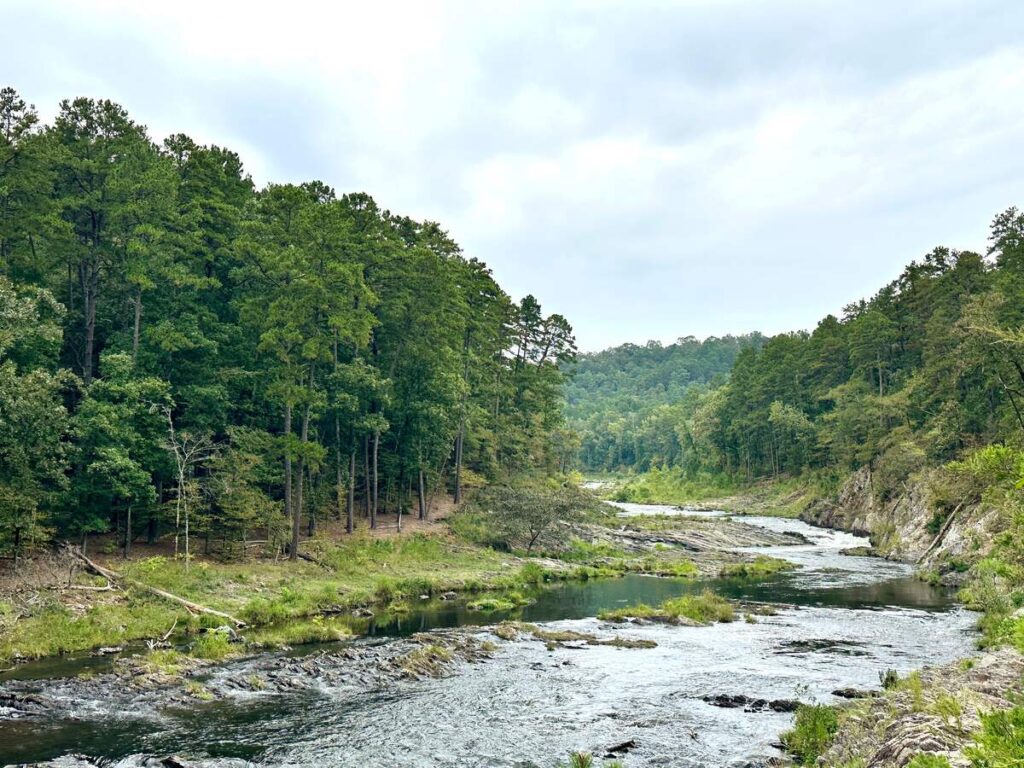 A beautiful view of the water surrounded by trees and a cloudy sky in Broken Bow, Oklahoma.