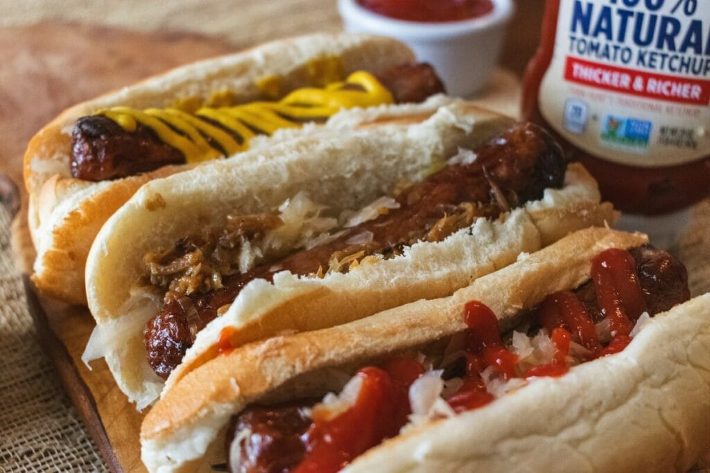 Three hotdogs laying side by side with various toppings.