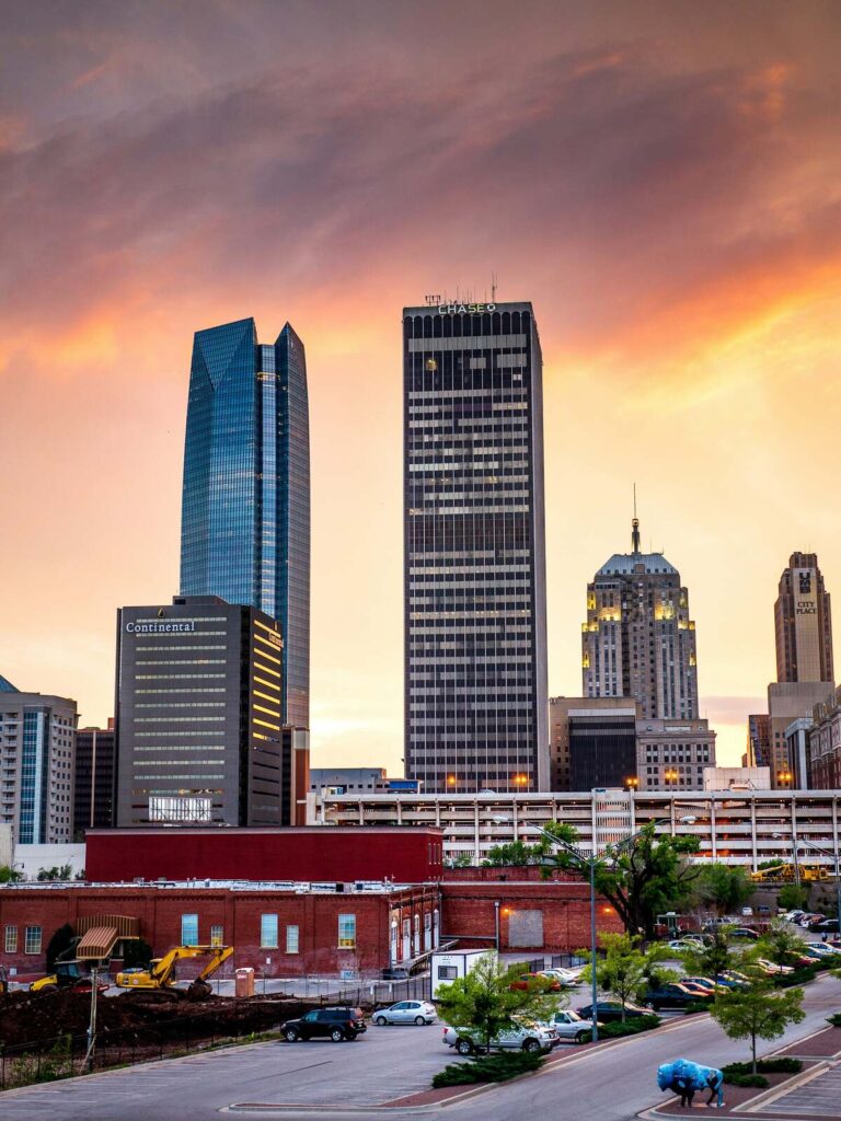 Views of the skyscrapers in downtown Oklahoma City with a setting sun behind them.